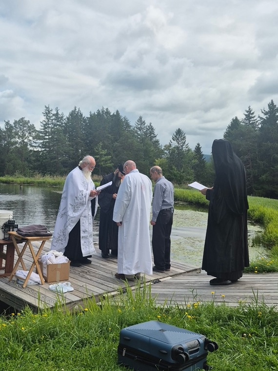 Clergy and the candidate gathered on a wooden dock at the pond for the baptism