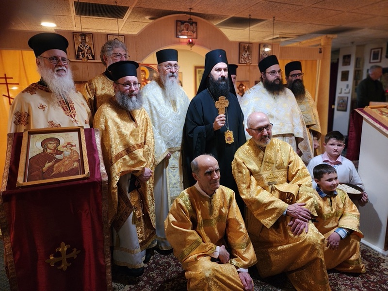 Clergy in gold vestments gathered with the bishop before an icon of the Mother of God, with two boys of the parish