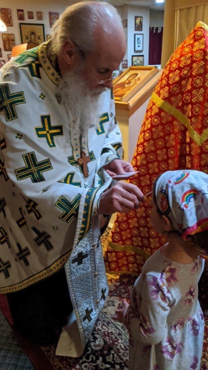 A priest in green-crossed vestments giving Communion to a small girl in a headscarf