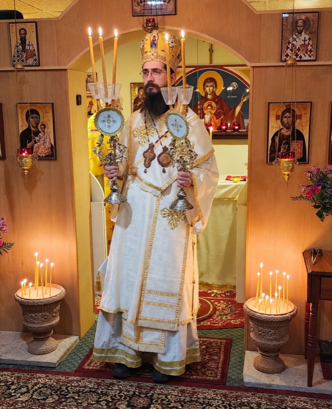 The bishop in white and gold vestments and mitre, holding the dikirion and trikirion between two stands of lit candles