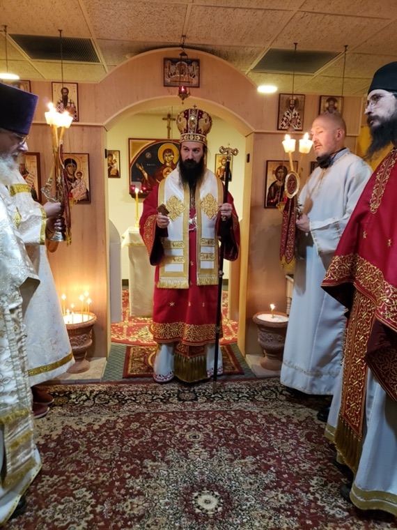 The bishop in red vestments and mitre censing in the chapel, flanked by clergy holding candles