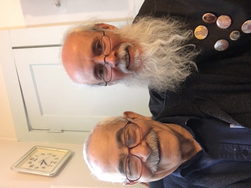 Two elderly parishioners smiling together, one a priest wearing icon medallions